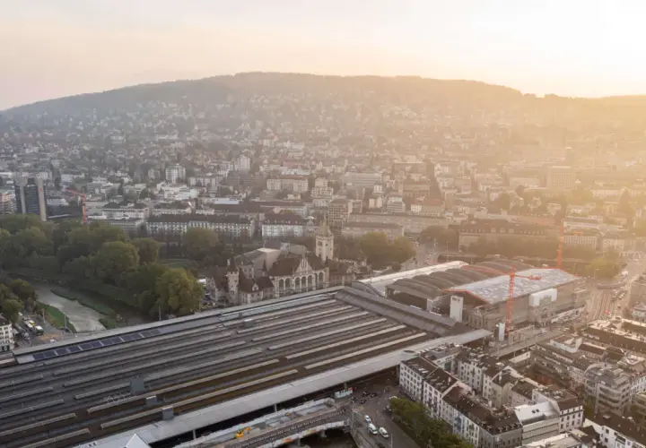 Luftaufnahme des Hauptbahnhofs Zürich bei Sonnenuntergang. Die vielen Gleise deuten darauf hin, welcher Bahnhof die meisten Gleise hat.