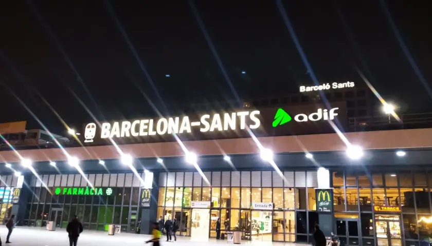Nachts leuchtet die Barcelona-Sants Hauptbahnhof-Fassade mit den Logos von McDonald's und Farmacia.