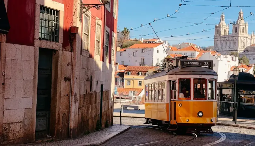 Gelber Straßenbahnwagen Nr. 28 fährt durch die engen Gassen Lissabons, vorbei an historischen Gebäuden und mit Blick auf die Basilika Estrela.
