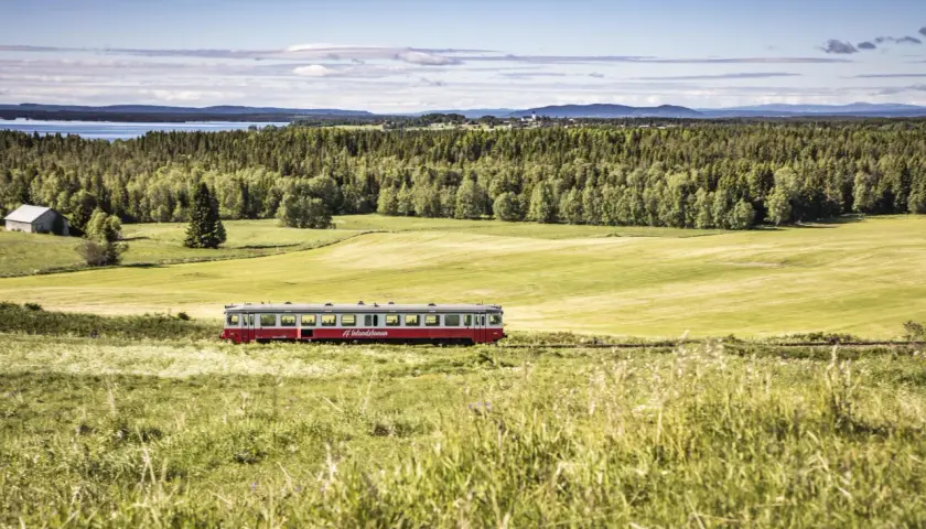 Ein roter Zug fährt durch eine grüne Landschaft in Schweden. Die #Inlandsbanan ist eine malerische Strecke.