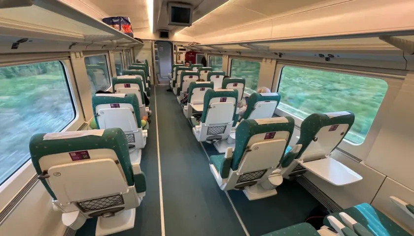 Innenraum eines Renfe Alvia Zuges mit grünen und weißen Sitzen, die auf einer Fahrt durch grüne Landschaften vorbeiziehen.