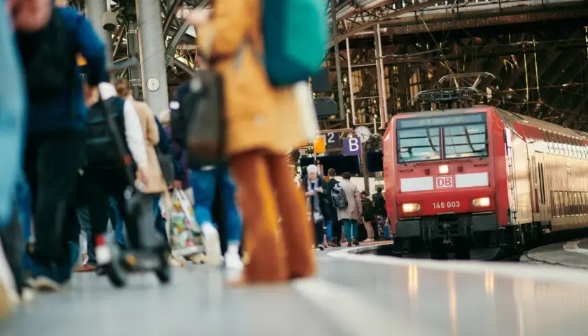 Menschen warten auf dem Bahnsteig auf ihre **Reise im Zug**. Eine rote Lokomotive der Deutschen Bahn steht bereit.