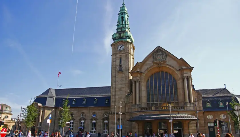 Der imposante **luxembourg train station** mit seinem Uhrturm und der großen Fensterfront, belebt von Reisenden unter blauem Himmel.