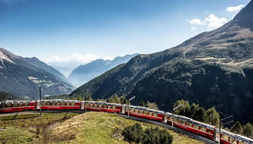 Der Bernina Express schlängelt sich **mit dem Zug durch die Schweiz** durch eine atemberaubende Berglandschaft.