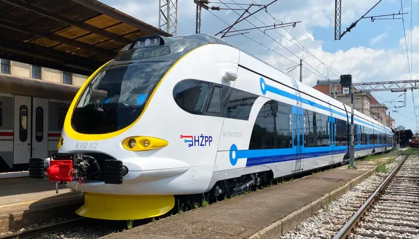 Moderner weiß-blauer kroatischer Zug (HŽPP) steht am Bahnsteig.