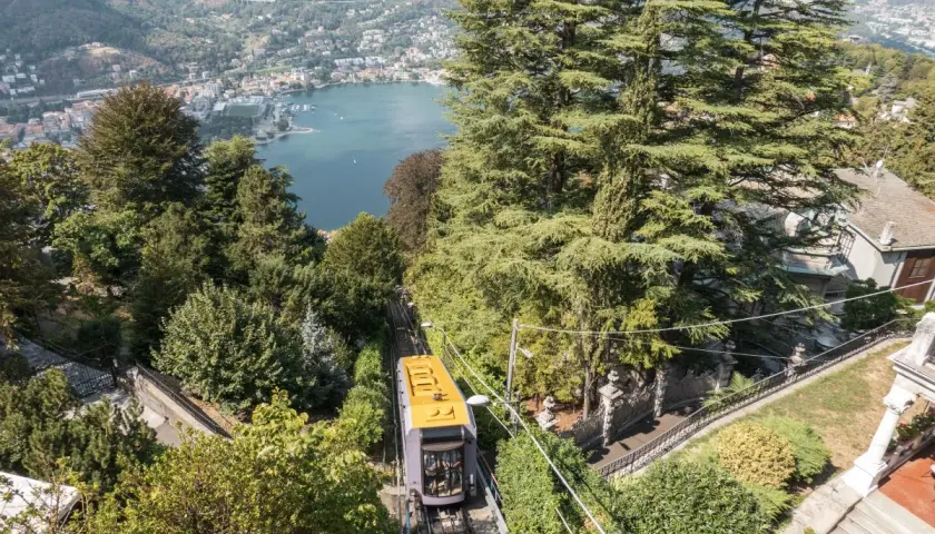 Gelbe Standseilbahn fährt bergauf, Blick auf Comer See und Bahnhof.