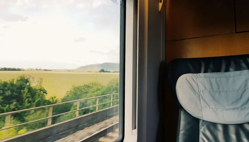 Blick aus dem Fenster eines Zuges auf dem Weg nach Hamburg. Grüne Felder und ein bewölkter Himmel ziehen vorbei.