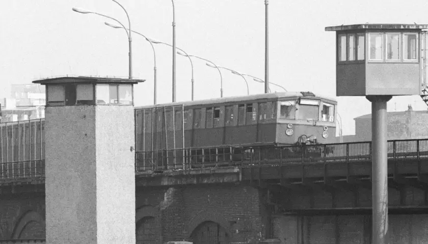 Eine Bahn fährt über eine Brücke, vorbei an Grenztürmen. Ein Symbol für die Zeit vor dem Mauerfall.