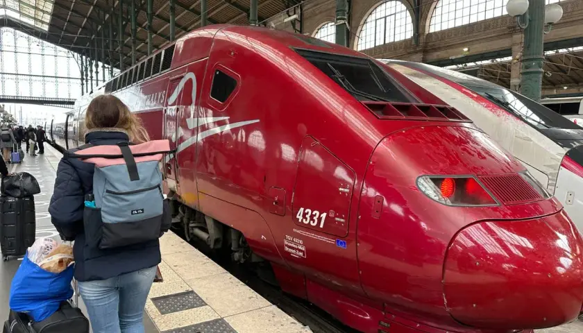 Roter Thalys-Zug am Bahnsteig, bereit für die Fahrt von Stuttgart nach Strasbourg. Eine Reisende mit Rucksack und Gepäck wartet.