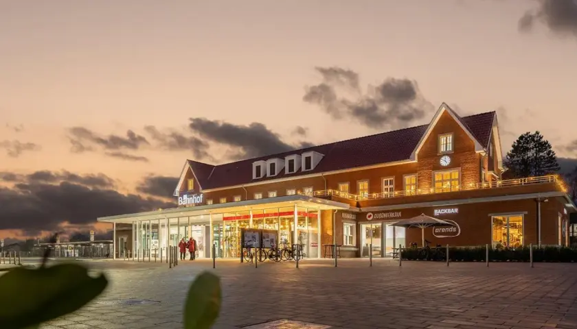 Der Bahnhof Nordhorn im Abendlicht, mit beleuchteten Fenstern und einem Schild "Bahnhof".