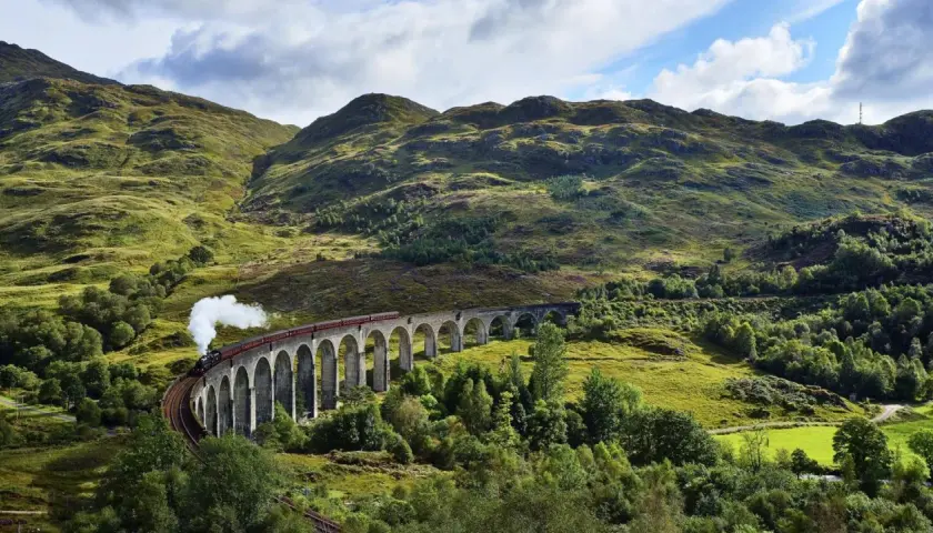 Dampfender Zug fährt über eine Bogenbrücke in den schottischen Highlands, auf dem Weg von Edinburgh in die malerische Landschaft.
