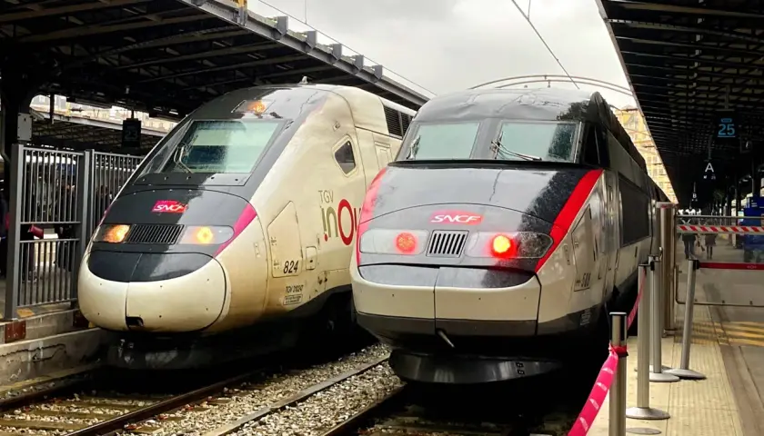 Zwei TGV-Züge stehen nebeneinander auf den Gleisen. Einer ist hellbeige mit der Aufschrift "TGV inOui", der andere ist dunkelgrau mit roten Akzenten. Sie warten auf ihre Abfahrt, vielleicht nach Paris von Luxemburg.