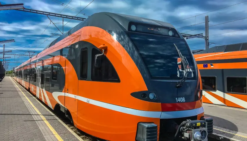Moderner, orange-grauer latvia train steht am Bahnsteig unter blauem Himmel mit Wolken.