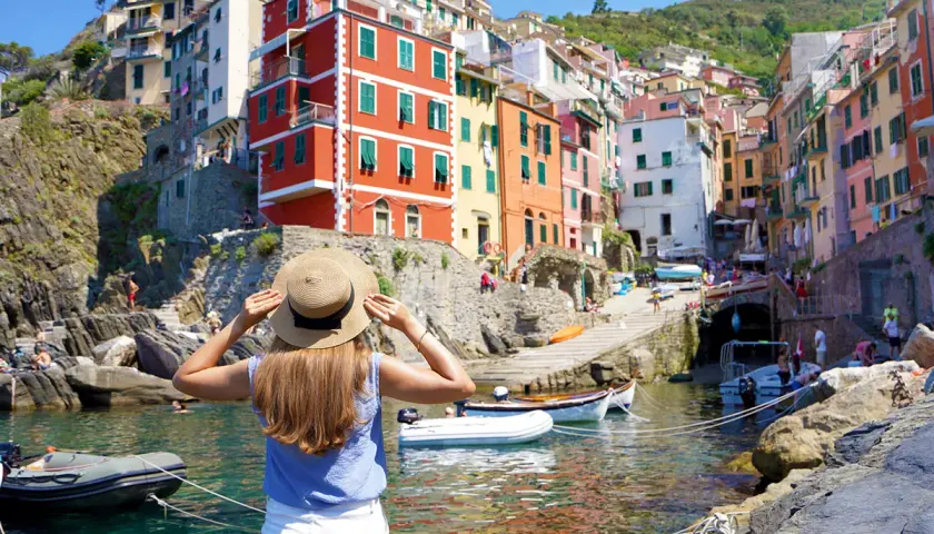 Frau mit Strohhut blickt auf bunte Häuser am Meer in Italien. Die Reise mit dem Zug ans Meer war die perfekte Idee für diesen Urlaub.