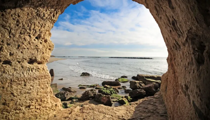 Blick aus einer Höhle am Strand von Rom. Wellen brechen an Felsen.