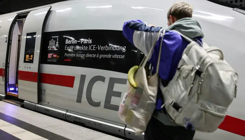 Ein Reisender mit Rucksack und Tasche steht vor dem ICE, der als "Berlin-Paris Erste direkte ICE-Verbindung" beworben wird.
