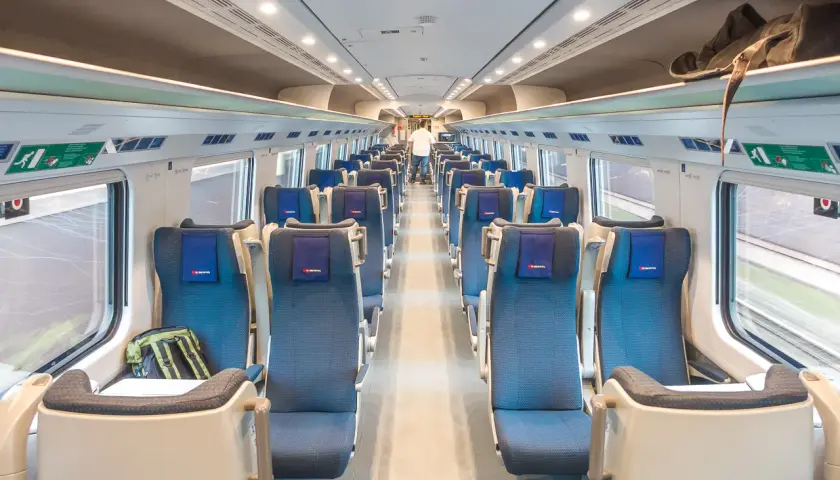 Innenraum eines modernen Euro City Express Zuges mit blauen Sitzen und Gepäckablagen.