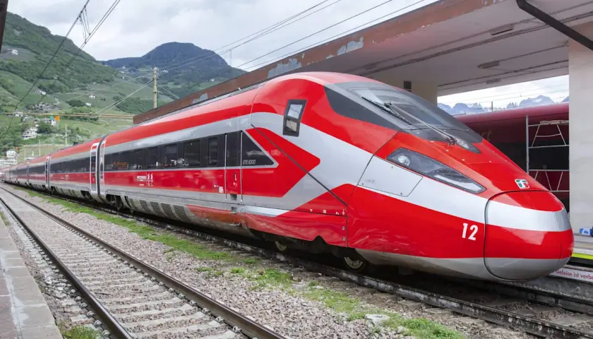 Roter Hochgeschwindigkeitszug mit silbernen Akzenten steht am Bahnsteig. Perfekt für eine entspannte Zug Rundreise durch die Berge.