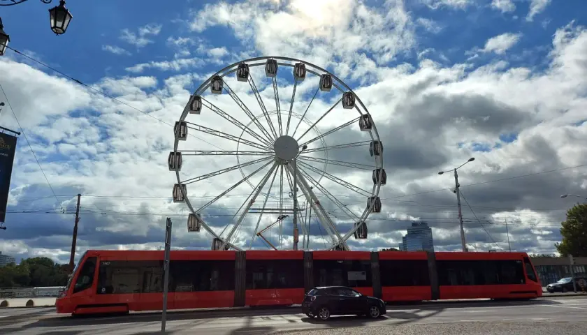 Rotes Tram fährt am Bratislava Hauptbahnhof vorbei, ein Riesenrad im Hintergrund.