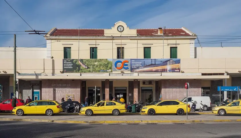 Gelbe Taxis warten vor dem Bahnhof Athen. Ein Schild verkündet "Wir transformieren unser Schienennetz, wir modernisieren Transporte".