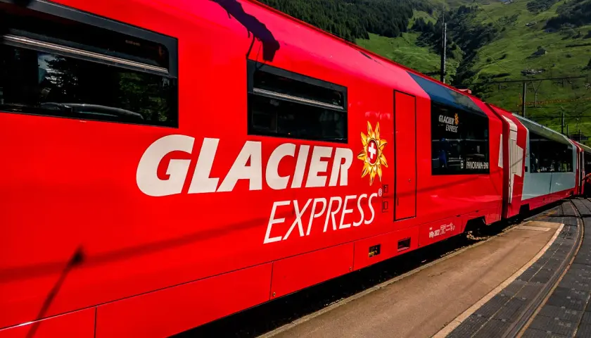 Der rote Glacier Express fährt durch eine grüne Berglandschaft.