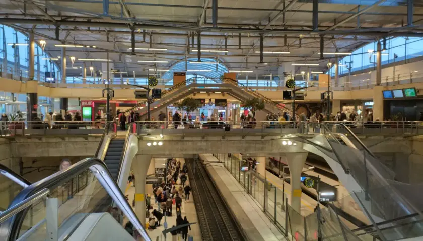 Menschenmassen auf einem Bahnhof, bereit für die Reise mit dem Zug nach Disneyland Paris. Rolltreppen und Bahnsteige sind voller Reisender.