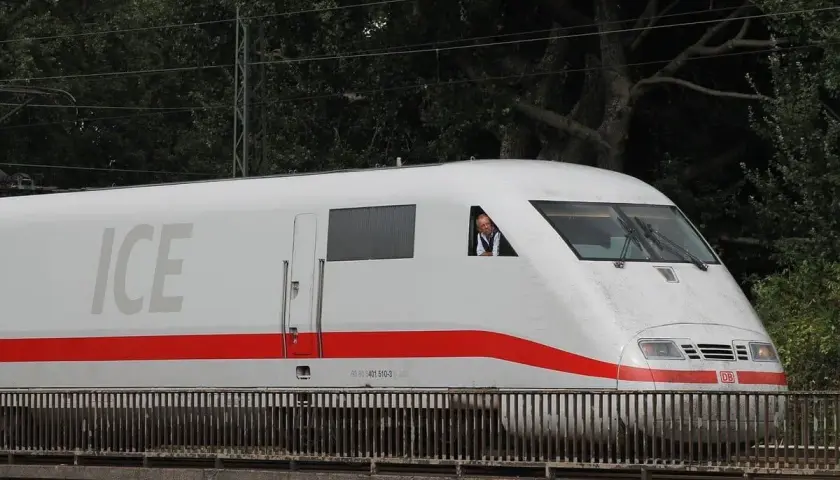 Ein Mann im Führerhaus eines weißen ICE-Zuges mit rotem Streifen. Der ICE-Service fährt auf einer Brücke.