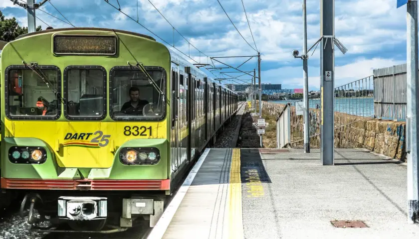 Grüner irischer Zug DART 25 mit der Nummer 8321 fährt auf einer Strecke am Meer entlang.
