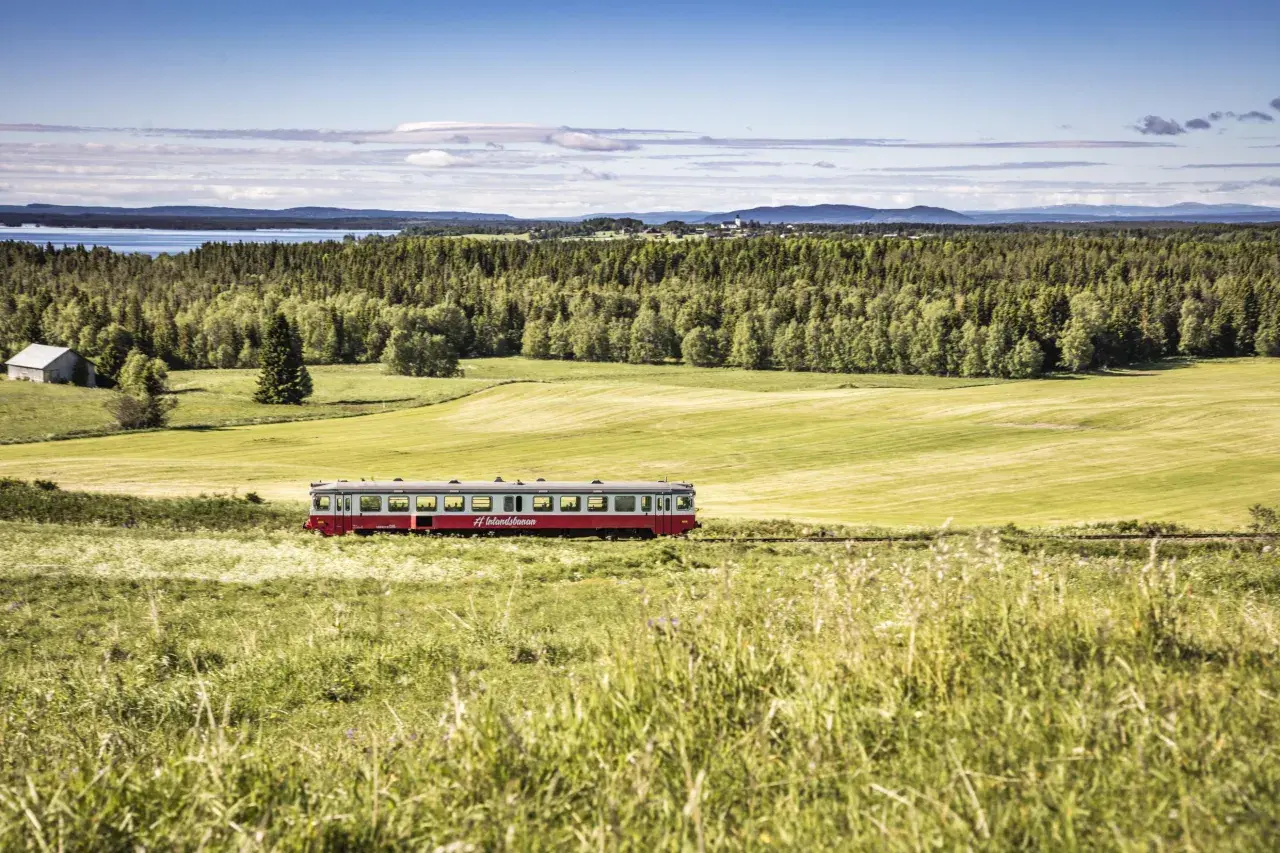 Ein roter Zug fährt durch eine grüne Landschaft in Schweden. Die #Inlandsbanan ist eine malerische Strecke.