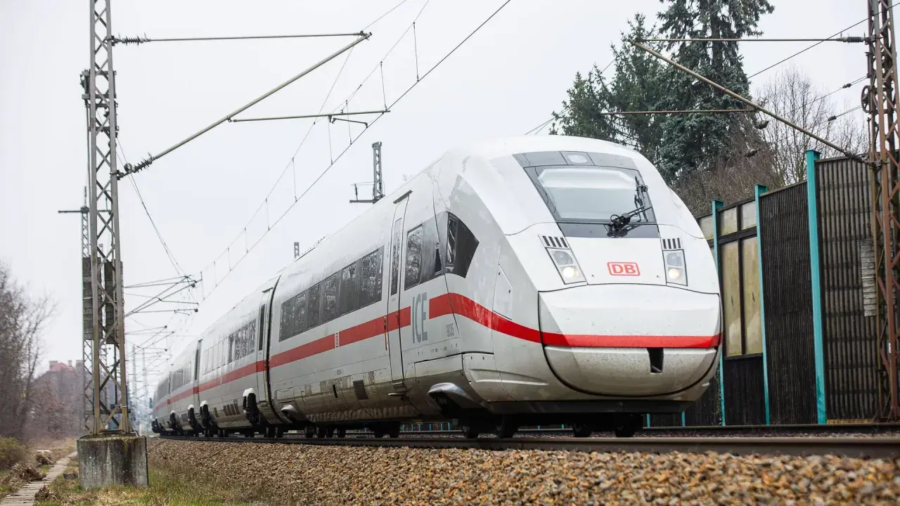 Moderner weißer ICE-Zug mit roten Streifen fährt auf Schienen. Eine Reise von Berlin nach Polen beginnt.
