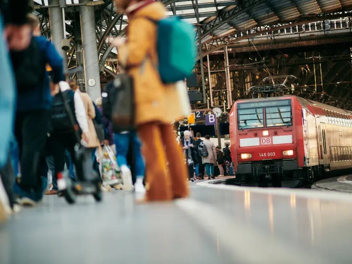 Menschen warten auf dem Bahnsteig auf ihre **Reise im Zug**. Eine rote Lokomotive der Deutschen Bahn steht bereit.