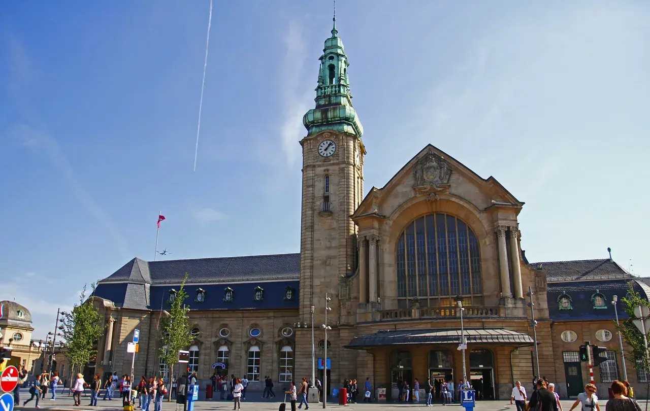 Der imposante **luxembourg train station** mit seinem Uhrturm und der großen Fensterfront, belebt von Reisenden unter blauem Himmel.