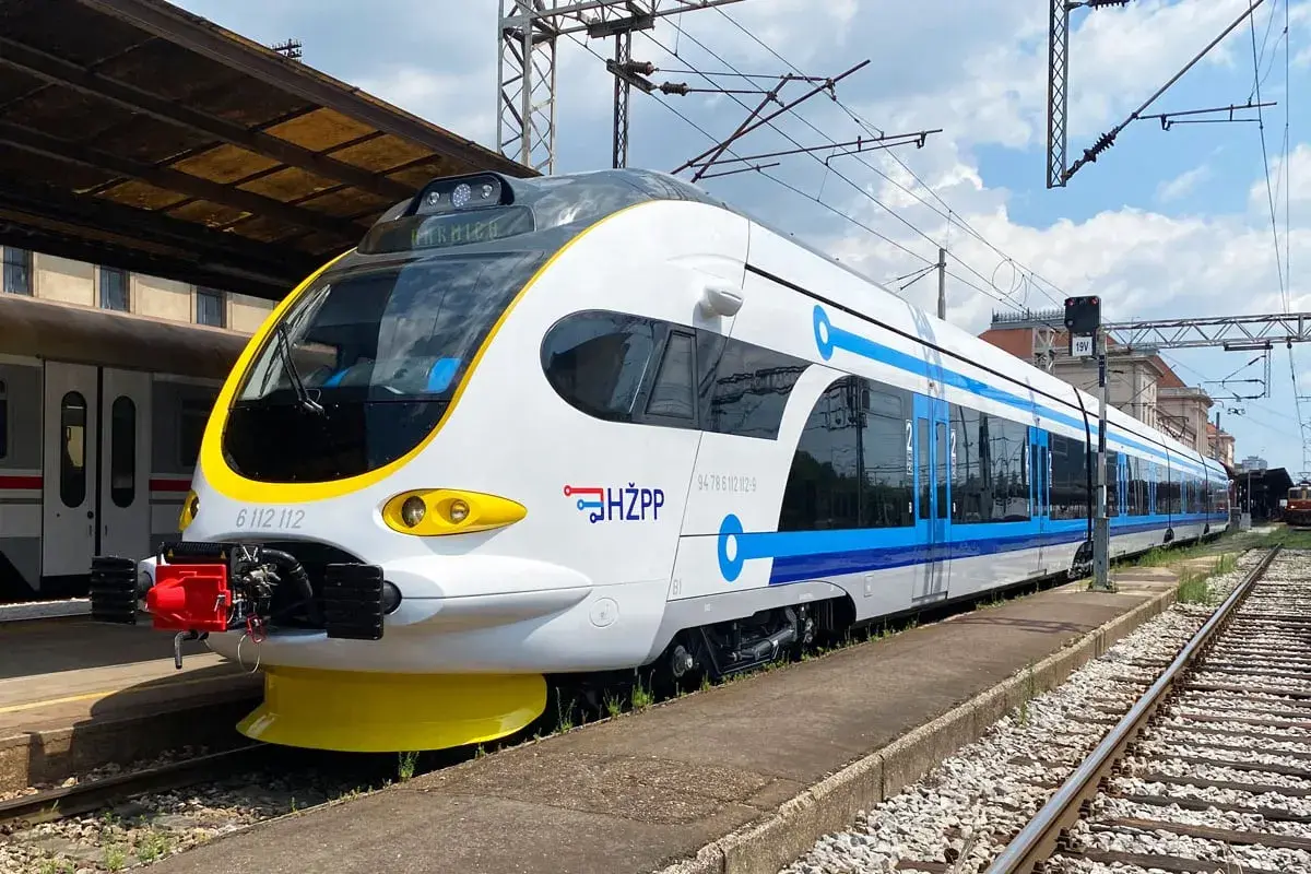 Moderner weiß-blauer kroatischer Zug (HŽPP) steht am Bahnsteig.