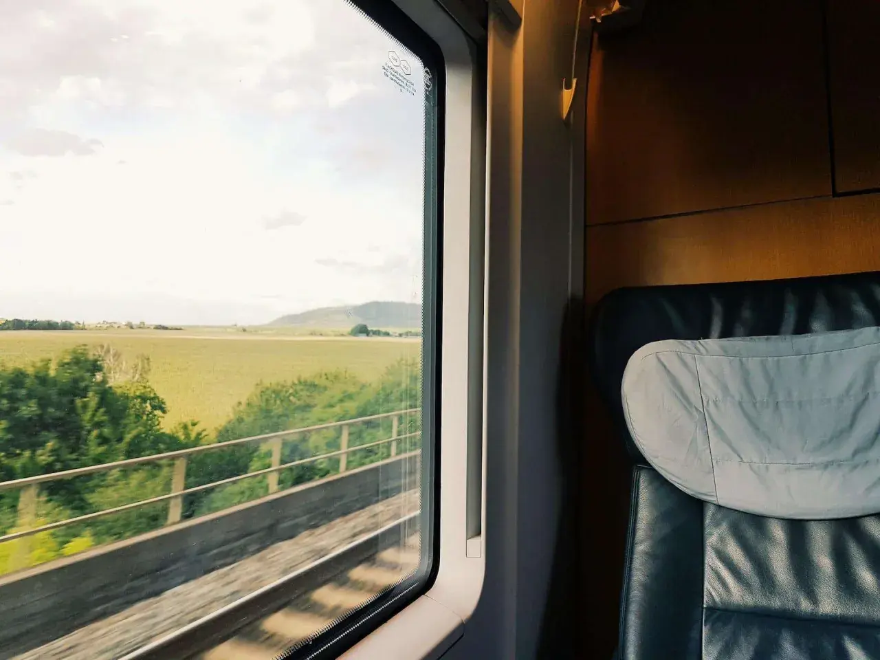 Blick aus dem Fenster eines Zuges auf dem Weg nach Hamburg. Grüne Felder und ein bewölkter Himmel ziehen vorbei.