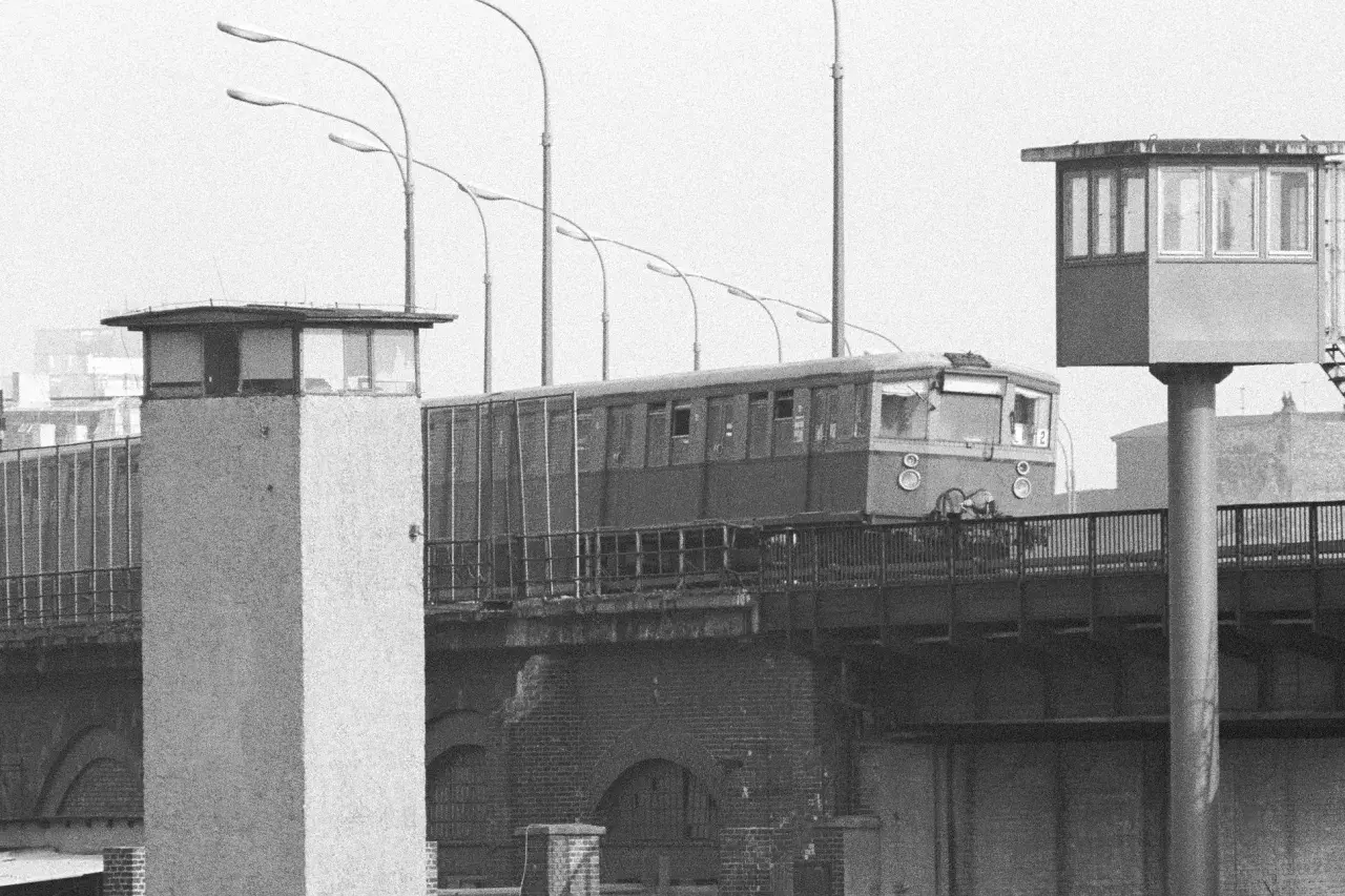 Eine Bahn fährt über eine Brücke, vorbei an Grenztürmen. Ein Symbol für die Zeit vor dem Mauerfall.
