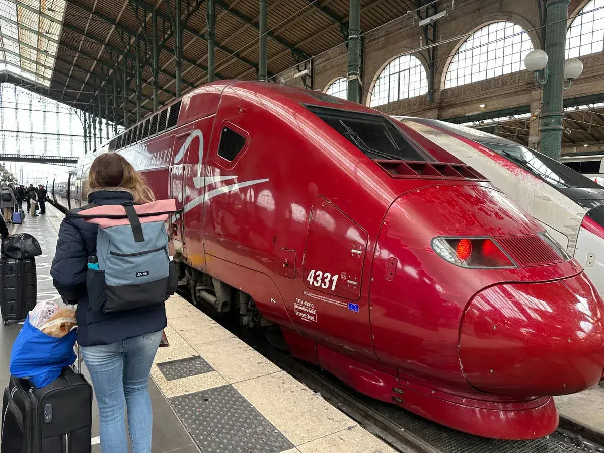 Roter Thalys-Zug am Bahnsteig, bereit für die Fahrt von Stuttgart nach Strasbourg. Eine Reisende mit Rucksack und Gepäck wartet.