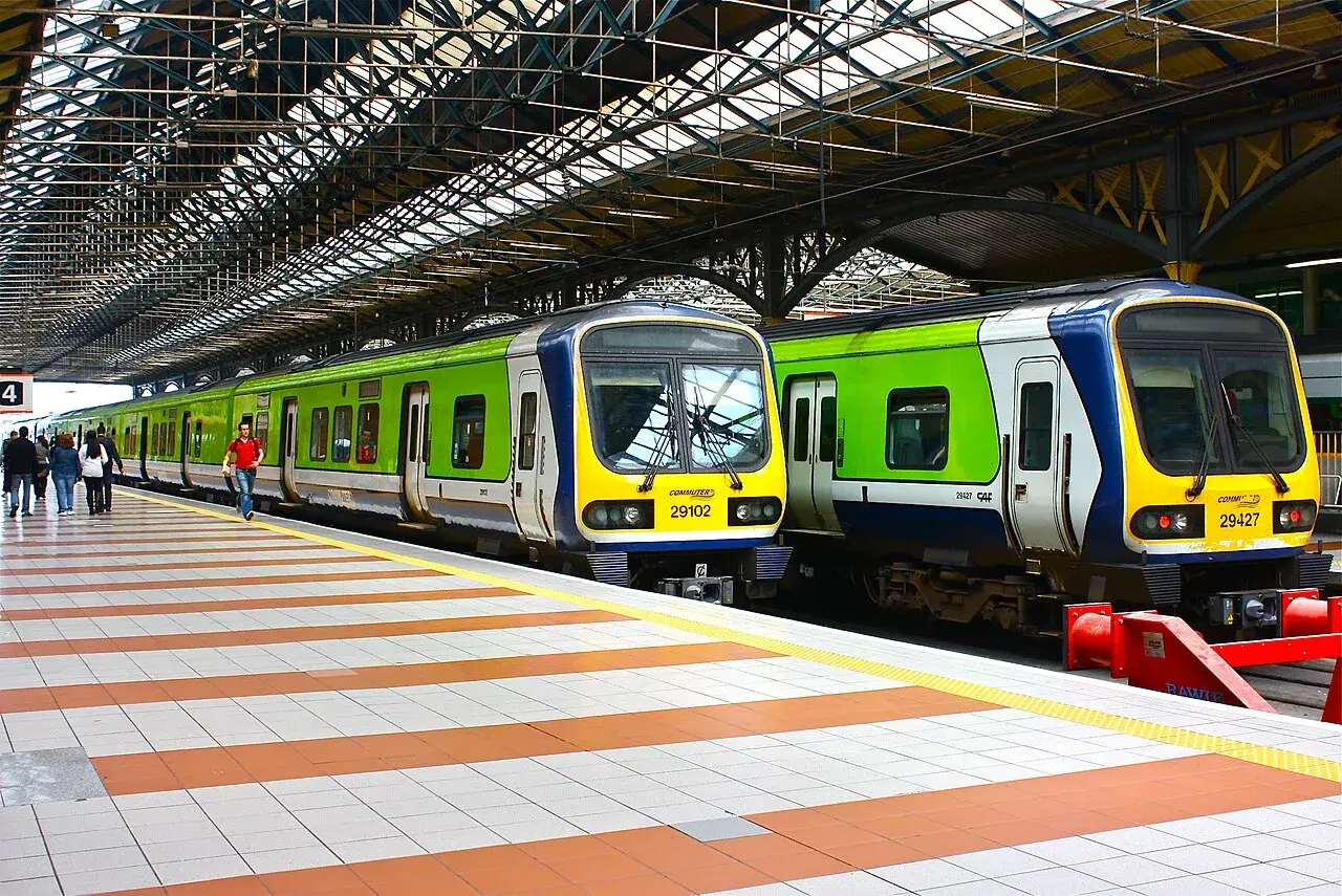 Zwei grüne und blaue Züge stehen auf einem Bahnsteig unter einem großen Dach.