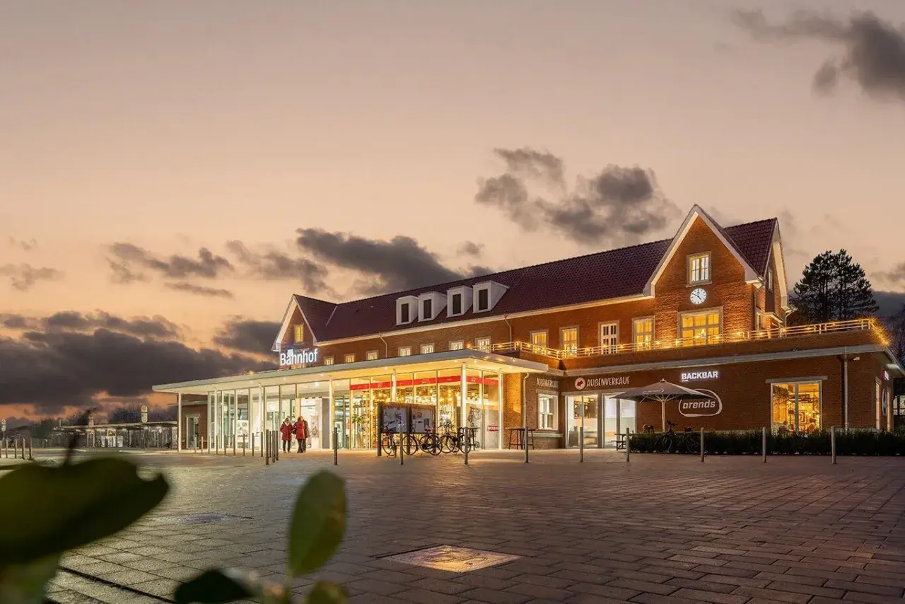 Der Bahnhof Nordhorn im Abendlicht, mit beleuchteten Fenstern und einem Schild "Bahnhof".