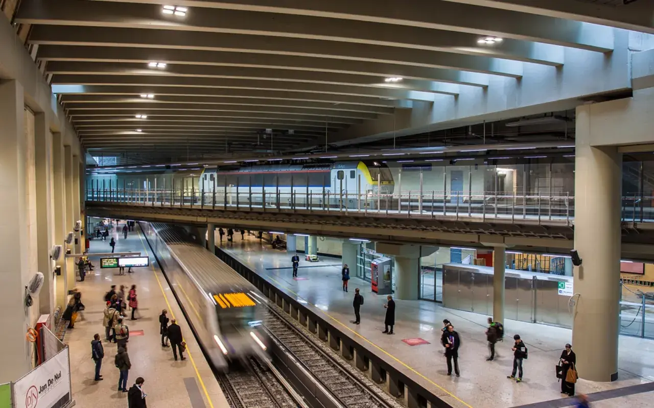 Moderne Züge fahren auf mehreren Ebenen im Brüsseler Bahnhof ein und aus. Reisende warten auf den Bahnsteigen.