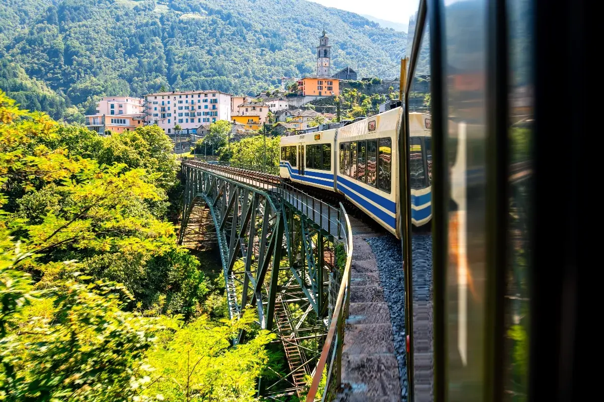 Mit dem Zug in die Toskana: Eine malerische Fahrt über eine Eisenbahnbrücke, vorbei an grünen Hügeln und einem charmanten Dorf mit Kirchturm.