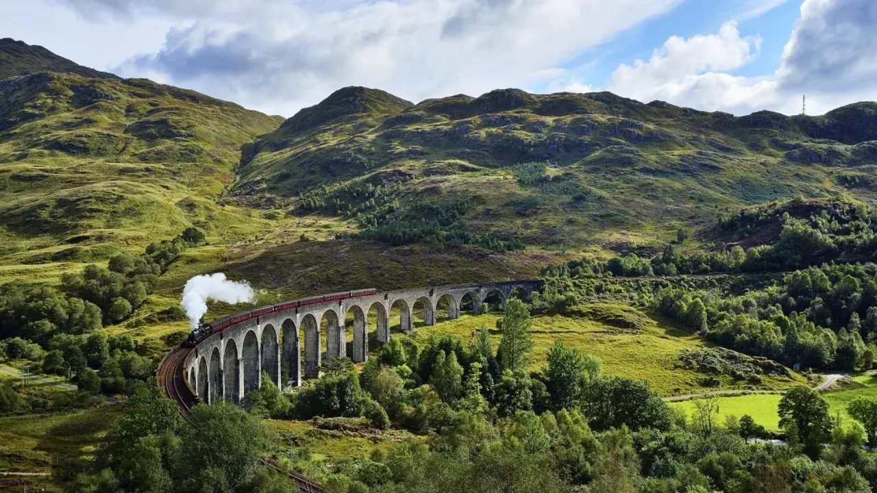 Dampfender Zug fährt über eine Bogenbrücke in den schottischen Highlands, auf dem Weg von Edinburgh in die malerische Landschaft.