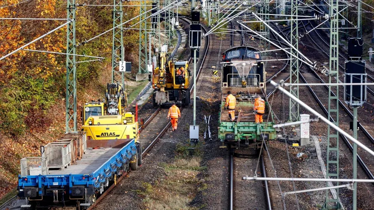Arbeiter in orangefarbenen Warnwesten inspizieren Gleise neben Baumaschinen und Zügen. Die Szene zeigt die Infrastruktur der serbischen Eisenbahnen im Herbst.