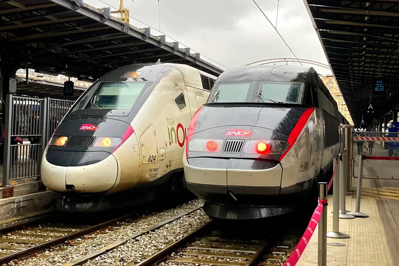 Zwei TGV-Züge stehen nebeneinander auf den Gleisen. Einer ist hellbeige mit der Aufschrift "TGV inOui", der andere ist dunkelgrau mit roten Akzenten. Sie warten auf ihre Abfahrt, vielleicht nach Paris von Luxemburg.