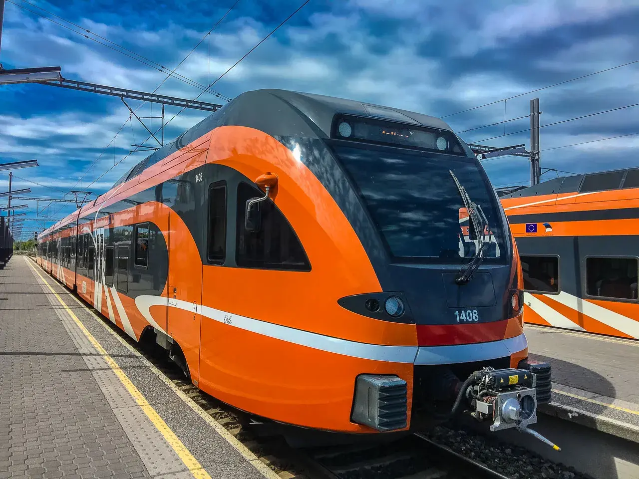 Moderner, orange-grauer latvia train steht am Bahnsteig unter blauem Himmel mit Wolken.