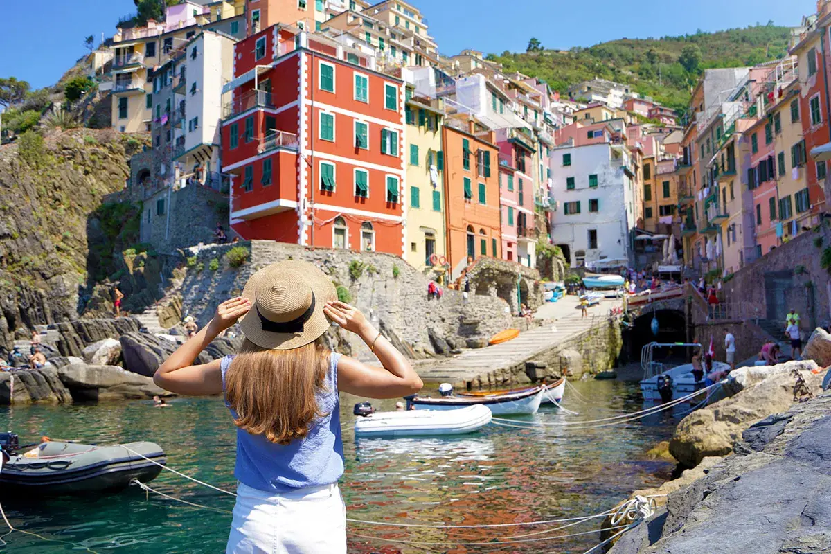 Frau mit Strohhut blickt auf bunte Häuser am Meer in Italien. Die Reise mit dem Zug ans Meer war die perfekte Idee für diesen Urlaub.
