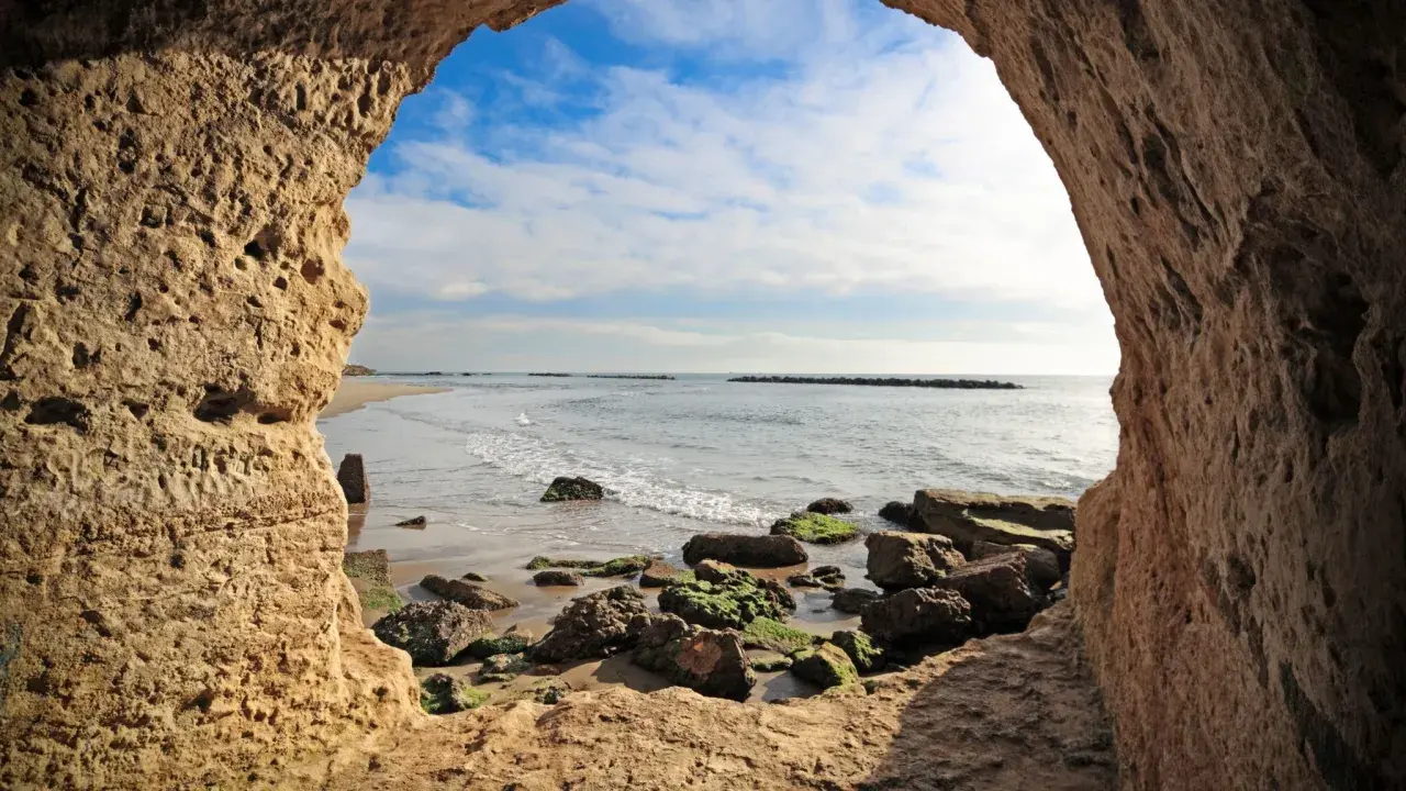 Blick aus einer Höhle am Strand von Rom. Wellen brechen an Felsen.