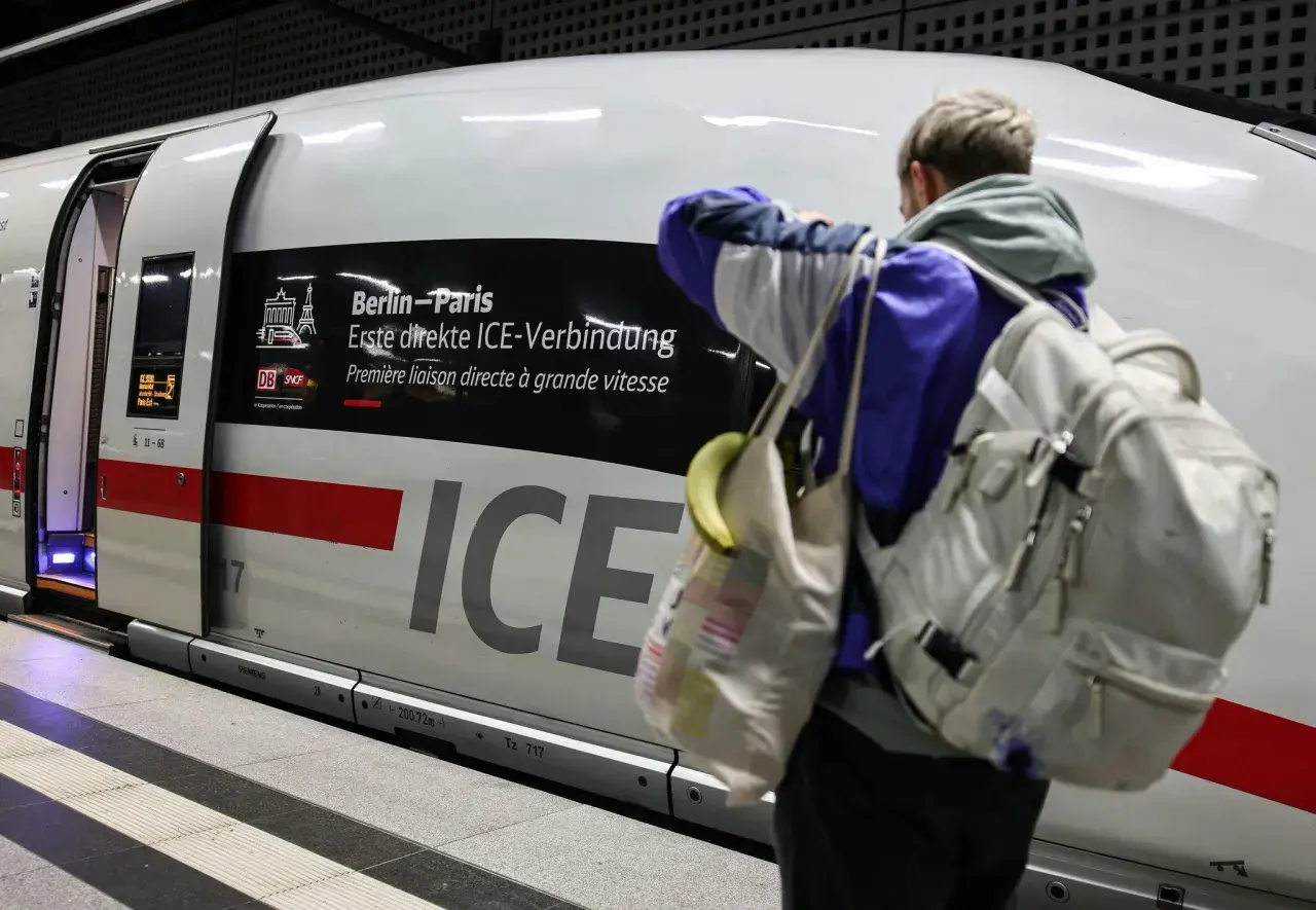 Ein Reisender mit Rucksack und Tasche steht vor dem ICE, der als "Berlin-Paris Erste direkte ICE-Verbindung" beworben wird.