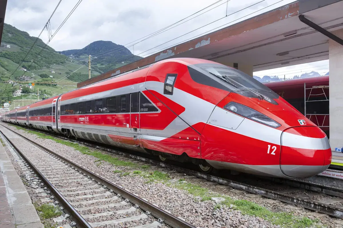 Roter Hochgeschwindigkeitszug mit silbernen Akzenten steht am Bahnsteig. Perfekt für eine entspannte Zug Rundreise durch die Berge.