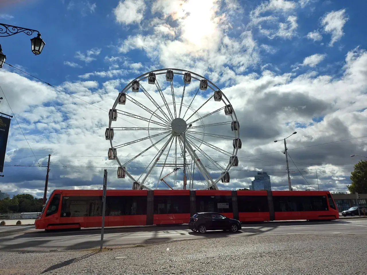 Rotes Tram fährt am Bratislava Hauptbahnhof vorbei, ein Riesenrad im Hintergrund.