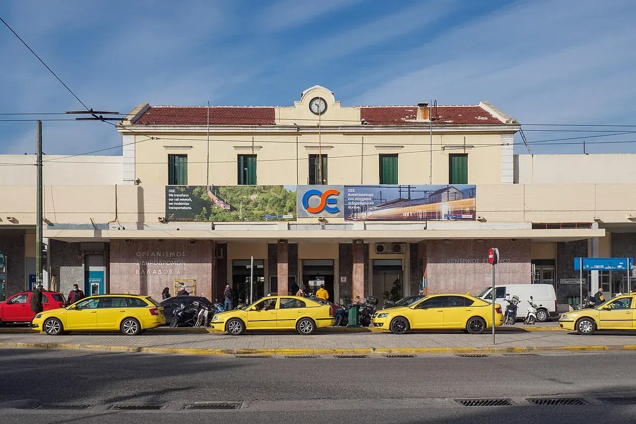 Gelbe Taxis warten vor dem Bahnhof Athen. Ein Schild verkündet "Wir transformieren unser Schienennetz, wir modernisieren Transporte".